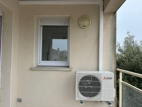 Unité extérieure de climatisation Mitsubishi fixée en façade de maison